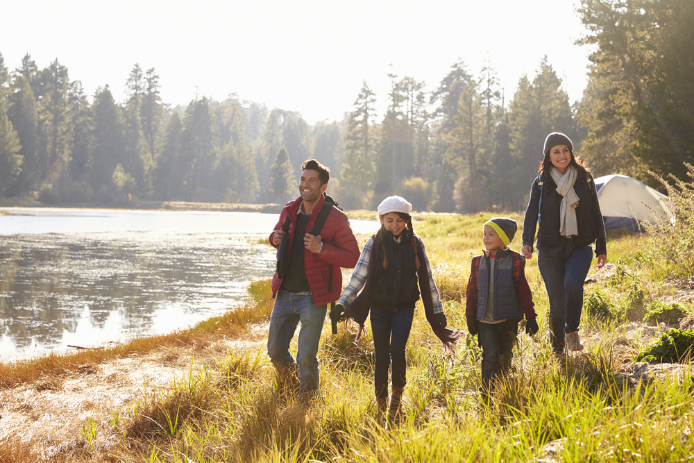 Mom, Dad, and two kids walking along lakeside with tent pitched in the background. 