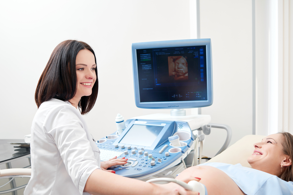 pregnant woman laying on doctor's table getting ultrasound done by female doctor with 3-D image of baby's face on the monitor